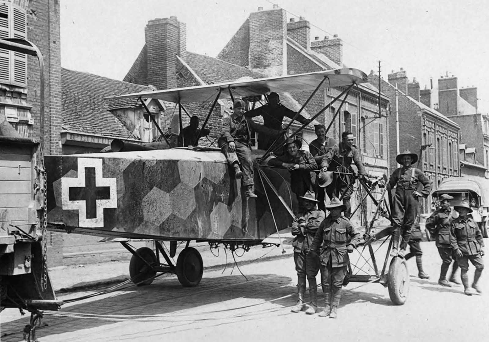 A downed German twin-engined bomber being towed through a street by Allied soldiers, likely from Australia, in France.