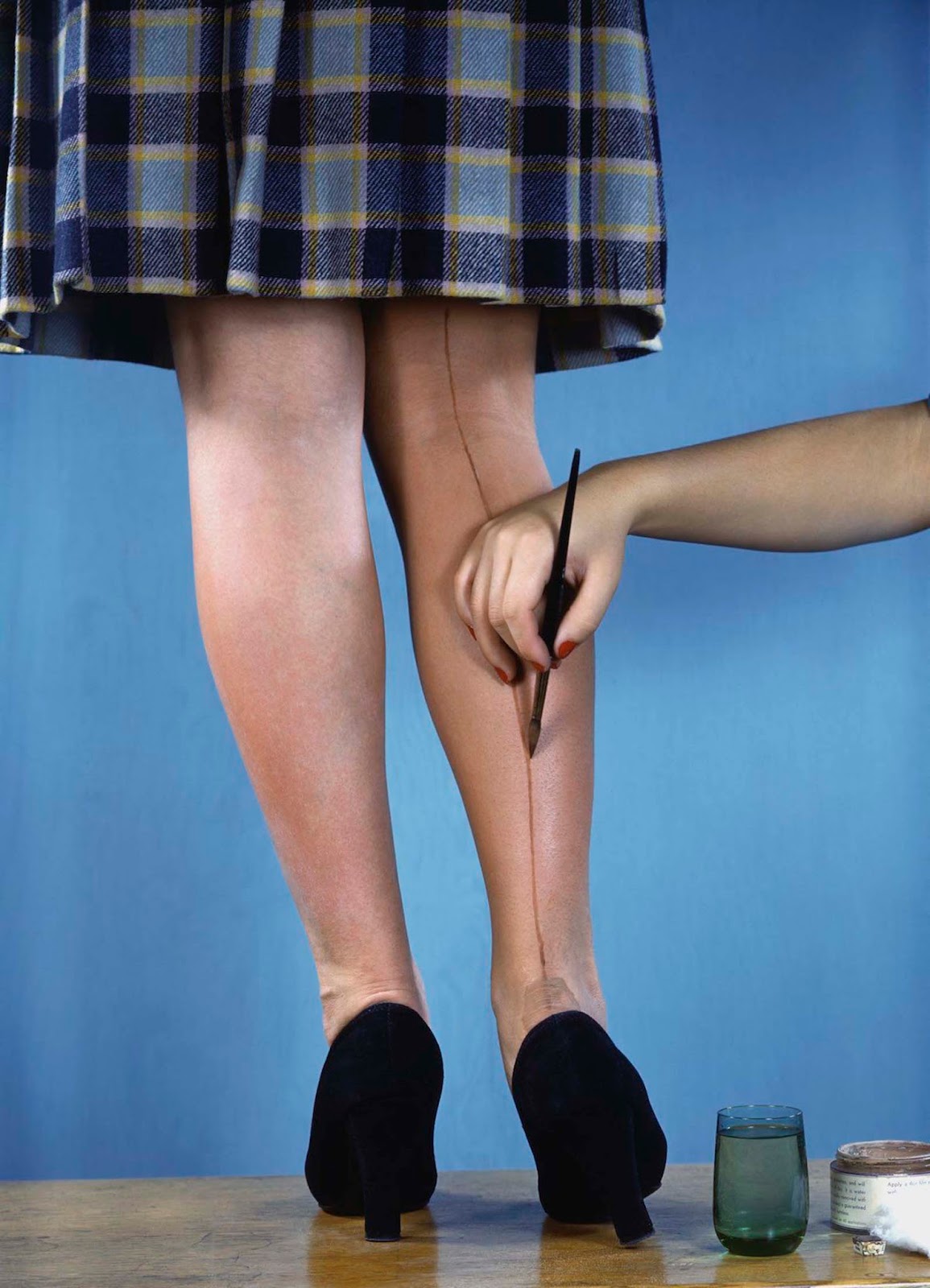 A woman painting the appearance of silk stockings onto another woman's legs. Very little silk was available during WWII in the U.S.