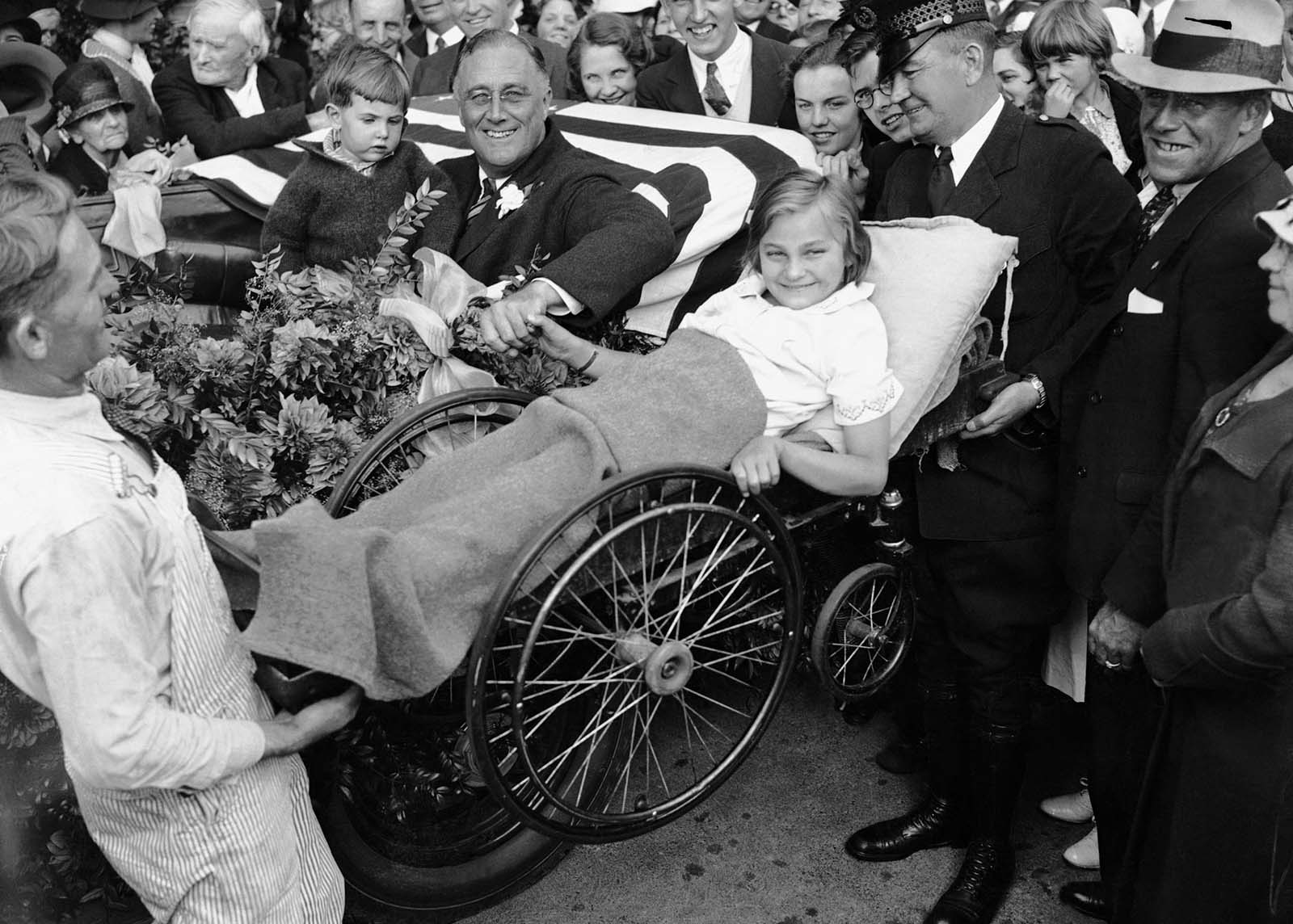 Franklin D. Roosevelt contracted polio in 1921 at age 39. Here, two men lift a little girl in a wheelchair so that Roosevelt can greet her from his vehicle during his first presidential campaign.