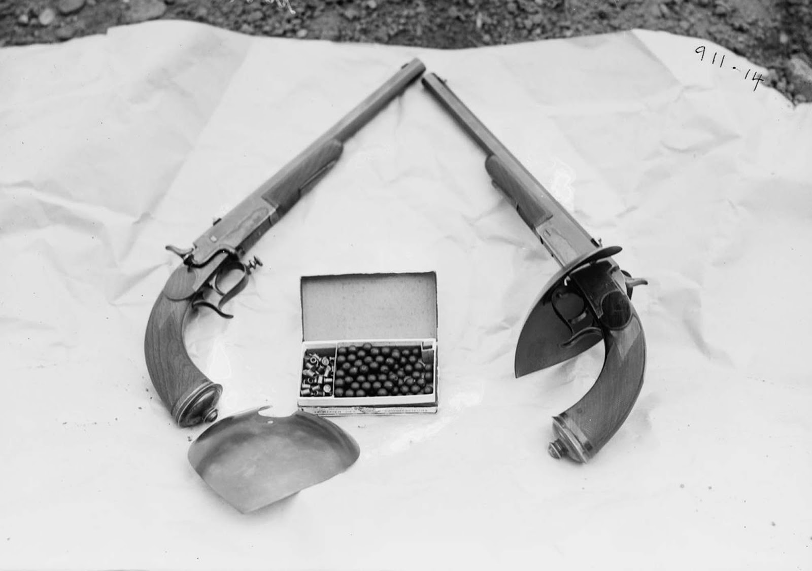 The modified .44caliber blackpowder pistols used in the 1909 exhibition. Note the handguard removed on left (showing mounting bracket), and fitted in place on right for comparison. The cartridge box in the center shows the outsized precussion caps, about the size of a .22 short on the left, and wax .44 diameter balls on the right.