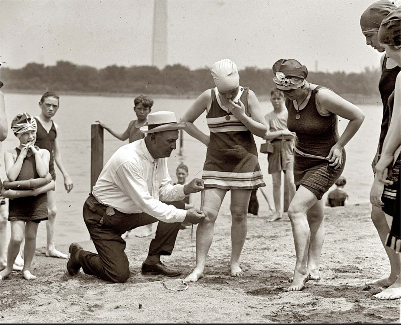 Washington policeman Bill Norton measuring the distance between knee and suit at the Tidal Basin bathing beach after Col. Sherrill, Superintendent of Public Buildings and Grounds, issued an order that suits not be over six inches above the knee. 1922.