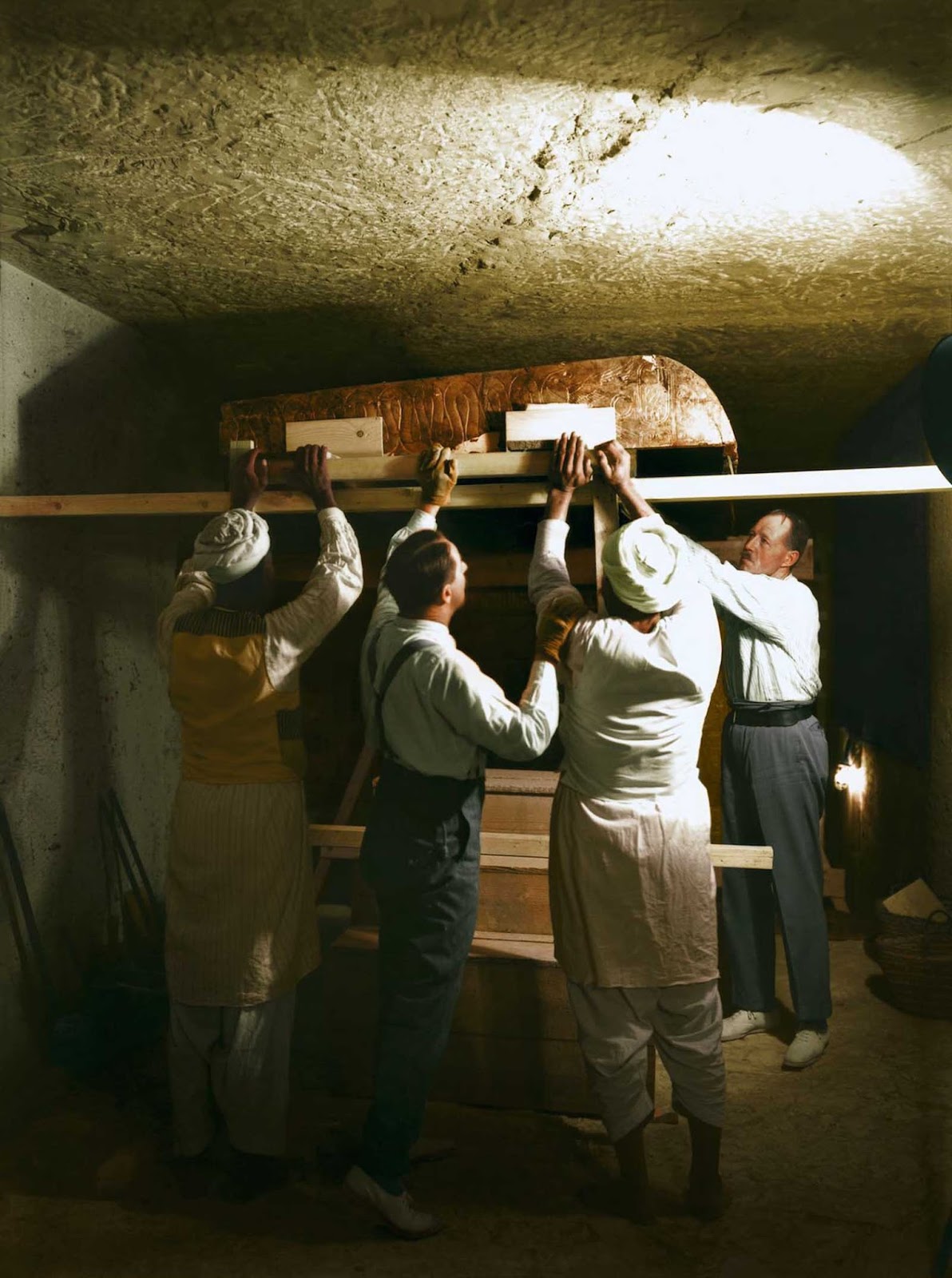 Carter, Callender and two Egyptian workers carefully dismantle one of the golden shrines within the burial chamber.