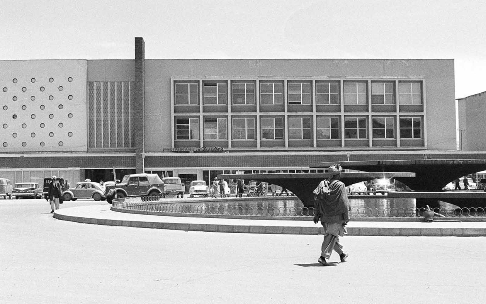 Modern new Finance Ministry building in Kabul, on June 9, 1966, with a public, western-style cafeteria and sidewalk restaurant, facing a water fountain which is illuminated in color at night.
