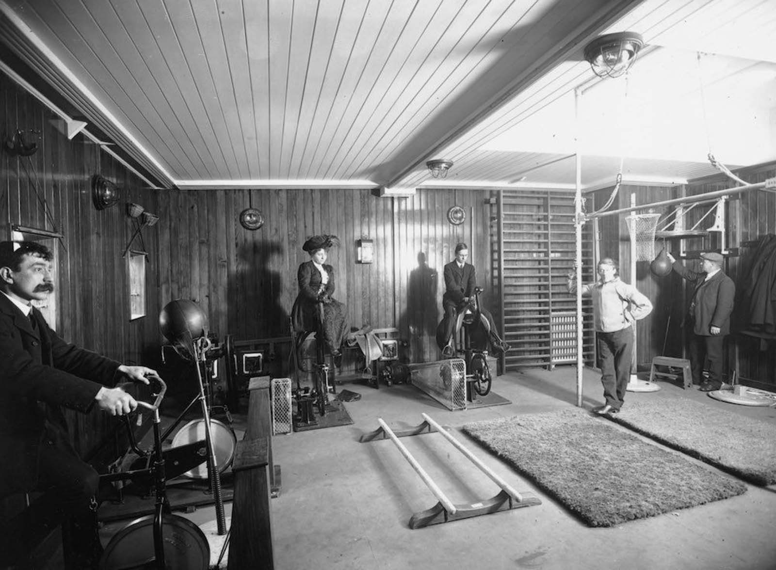 Edwardians riding exercise bikes whilst wearing day clothes in a gymnasium on board the Cunard line liner, RMS Franconia. Feb 21, 1911.