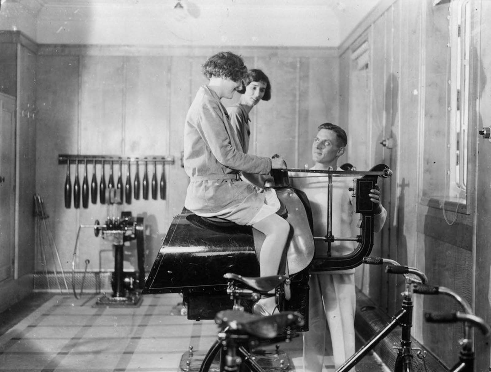 Passengers on the Canadian Pacific liner Duchess of Bedford keep fit in the ship's gymnasium, with the help of a riding machine. 1931.