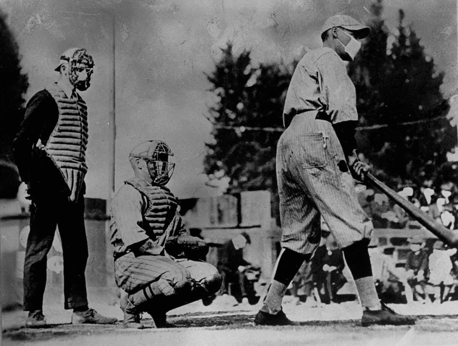 Unident baseball players, one batting and one catching, plus an umpire behind the plate, wear flu masks. 1918.