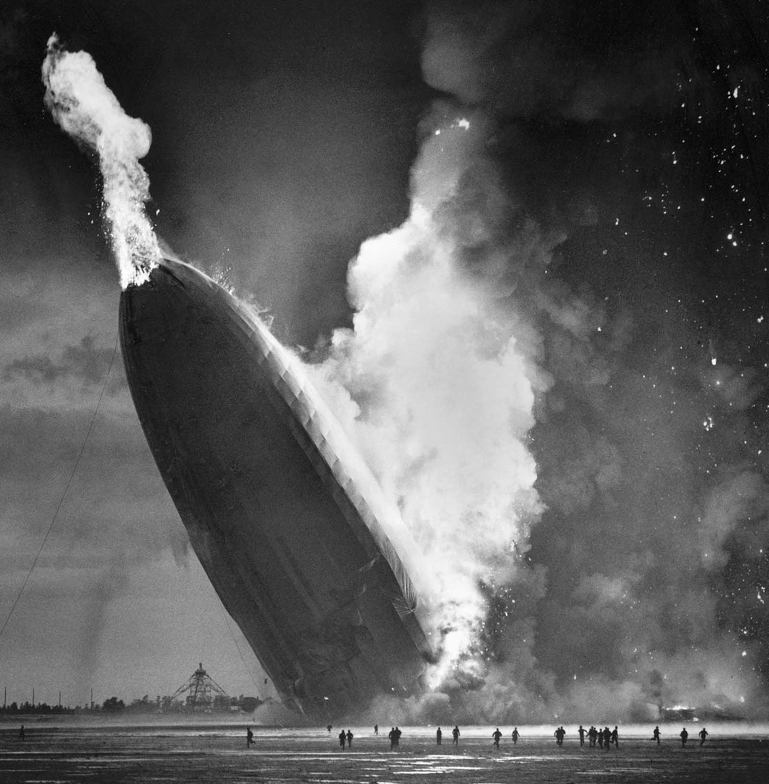 As the lifting Hydrogen gas burned and escaped from the rear of the Hindenburg, the tail dropped to the ground, sending a burst of flame punching through the nose. Ground crew below scatter to flee the inferno.