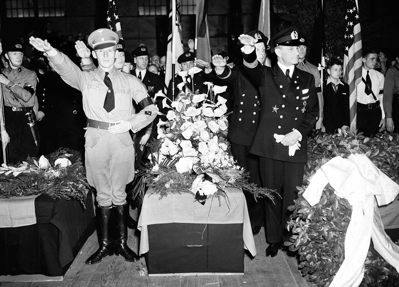 German soldiers give the salute as they stand beside the casket of Capt. Ernest A. Lehmann, former commander of the zeppelin Hindenburg, during funeral services held on the Hamburg-American pier in New York City, on May 11, 1937. The swastika-draped caskets were placed on board the SS Hamburg for their return to Europe.