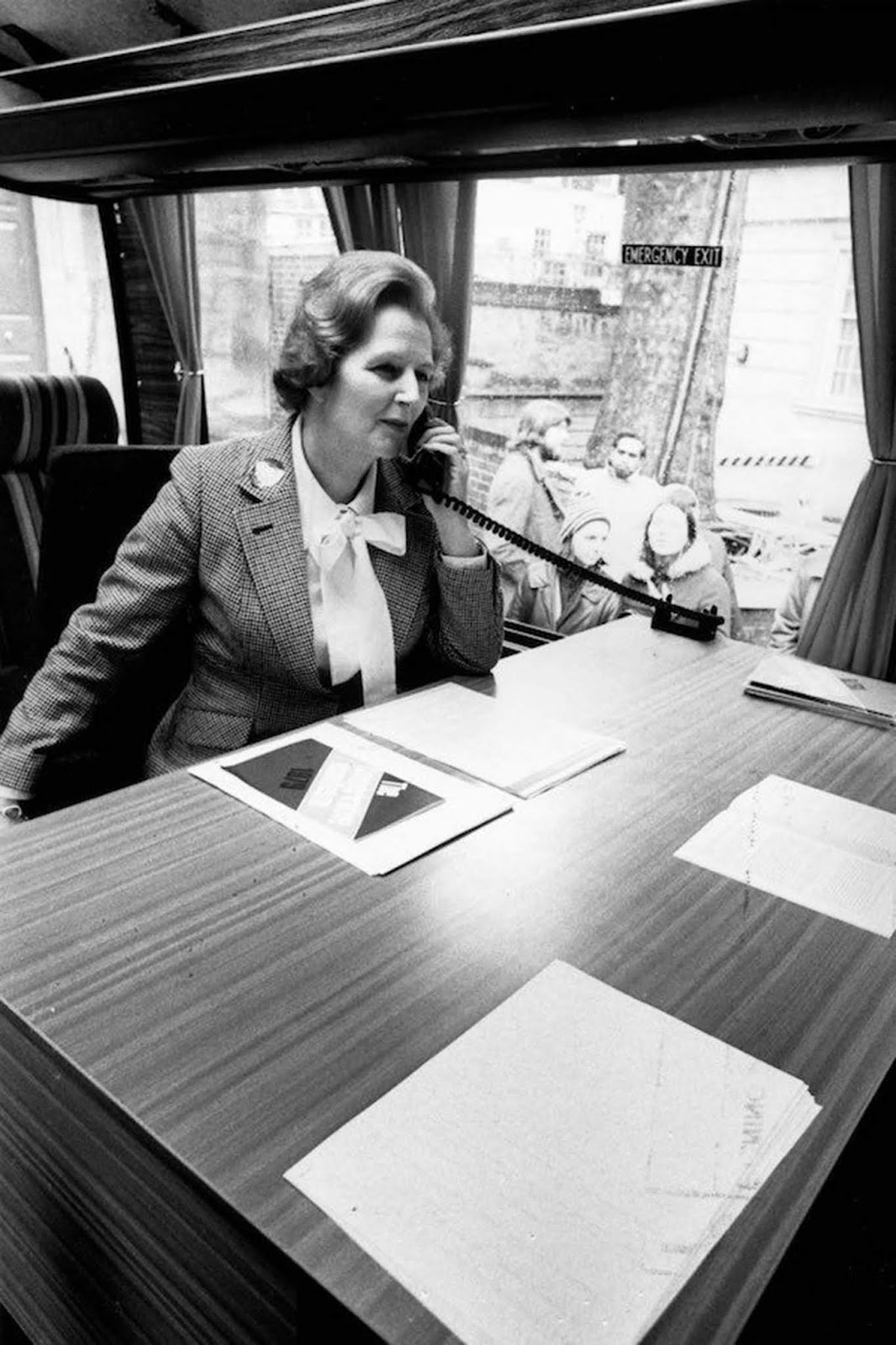 Margaret Thatcher making a telephone call in the Conservative Party coach during her election campaign. She wears a checked jacket and a blouse tied with a large bow. Her hair has a strong wave. 1979.
