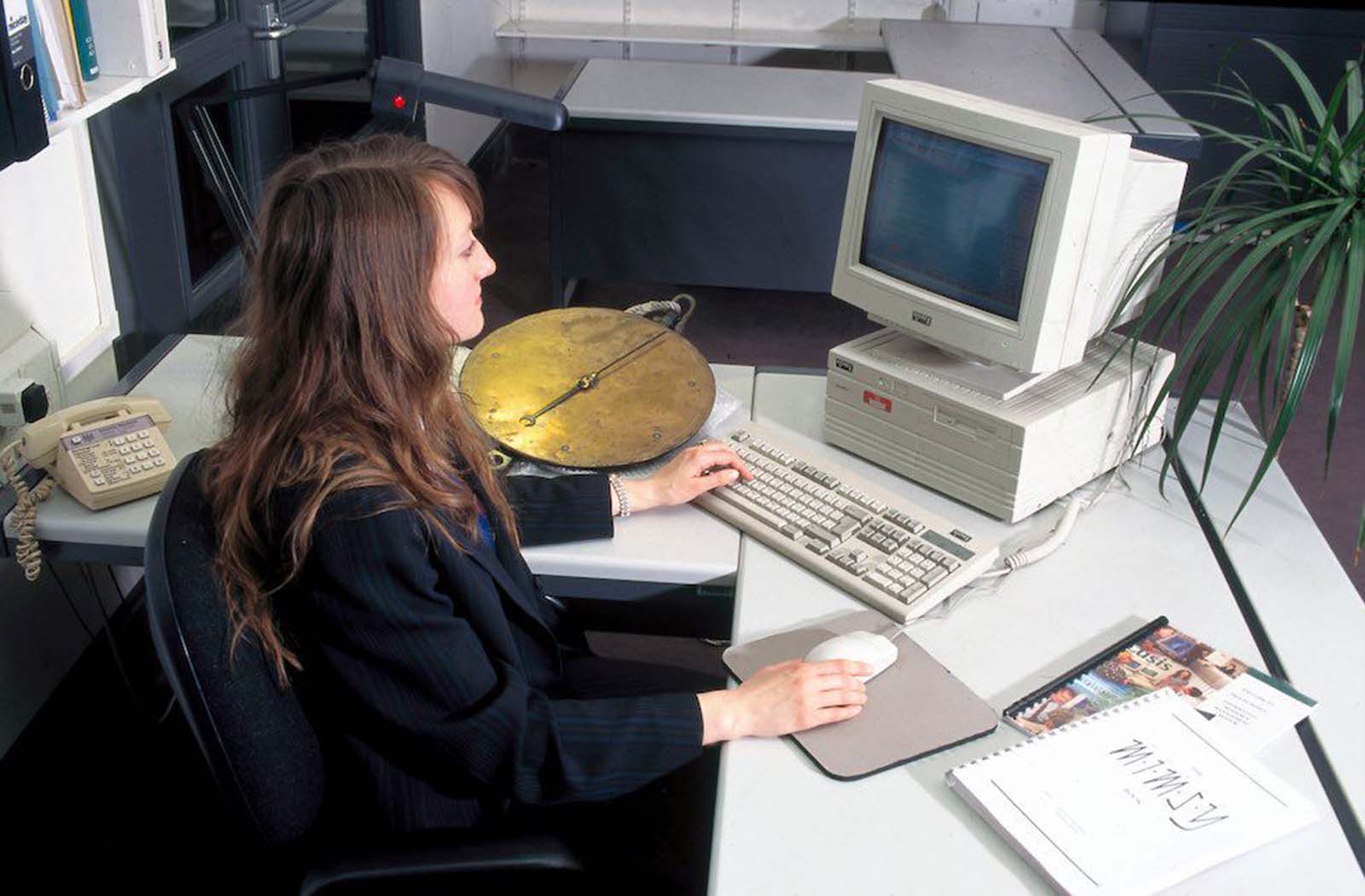 Sue Julian-Ottie, a collections system data manager, using a database computer. Her hair is long and natural, with side-swept bangs. She wears a dark, striped suit jacket. 1996.