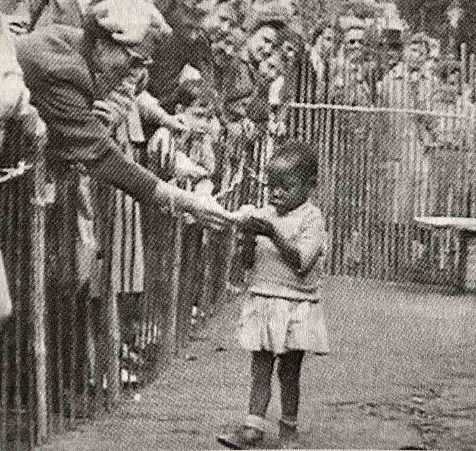 An African girl is shown at the 1958 Expo in Brussels, Belgium that featured a 'Congo Village' with visitors watching her from behind wooden fences.