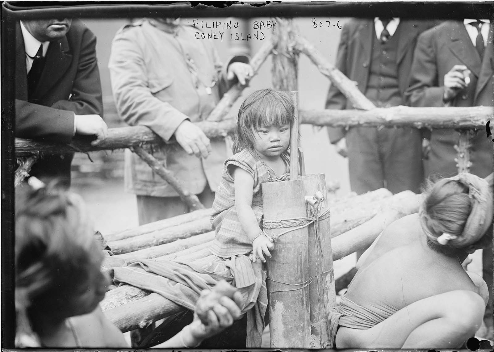 A young Filipino girl is pictured sitting on a wooden bench in an enclosure in Coney Island, New York in another horrifying 1906 'exhibit'.