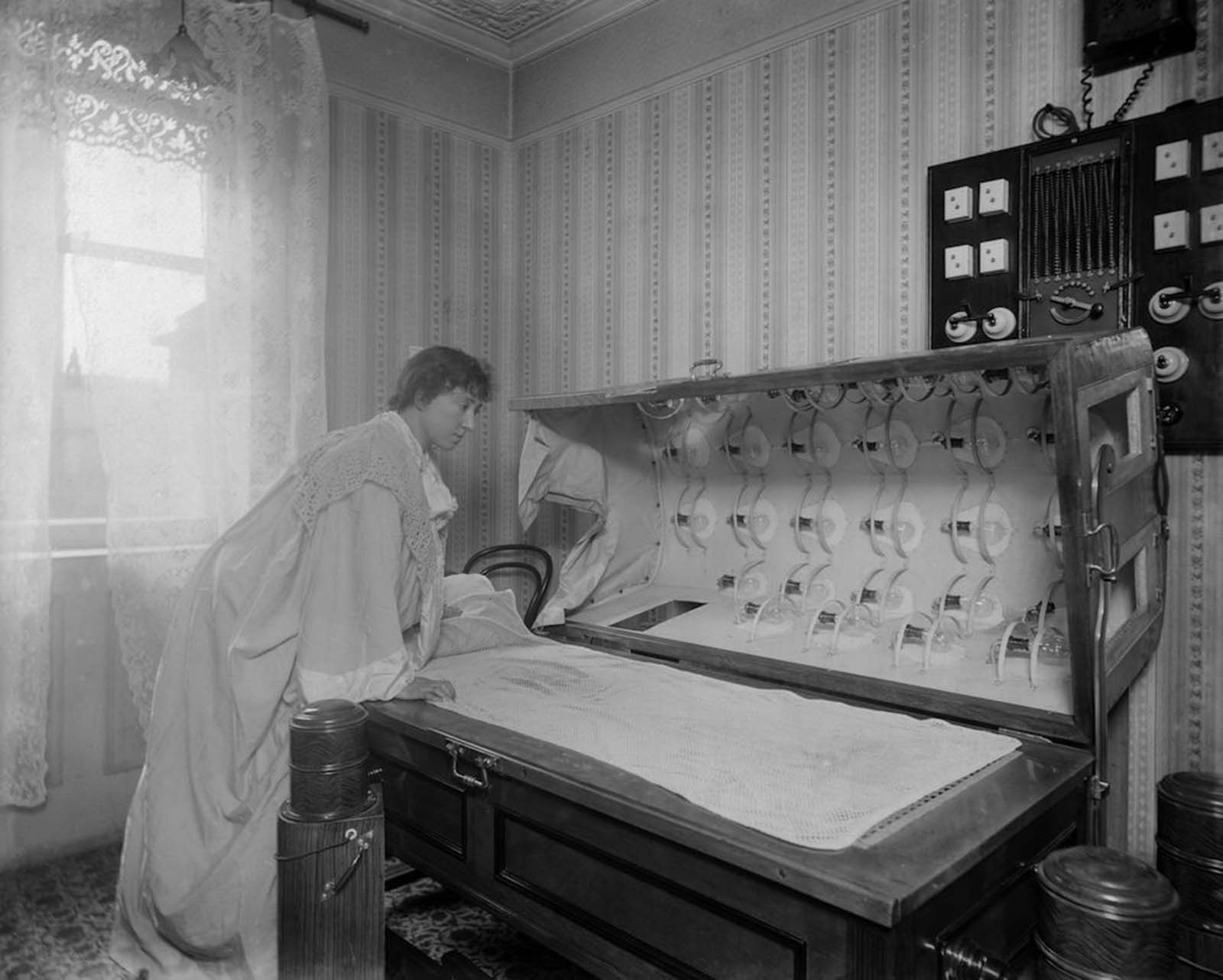 A woman inspects an Electric Bath at the Light Care Institute. The Electric Bath is probably a forerunner of the modern sunbed, although it was more likely used for medicinal reasons. Circa 1900.