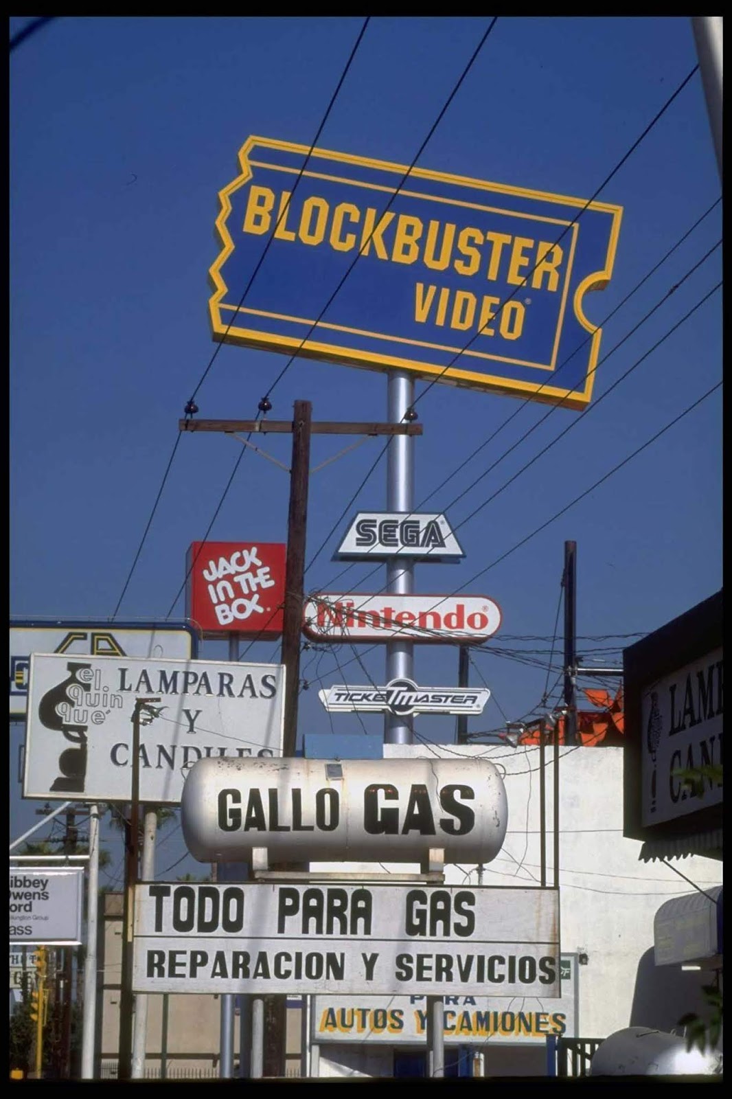 Blockbuster Video store & Jack In The Box fast food eatery among Amer. & Mexican services & products advertised on street signs in border town.