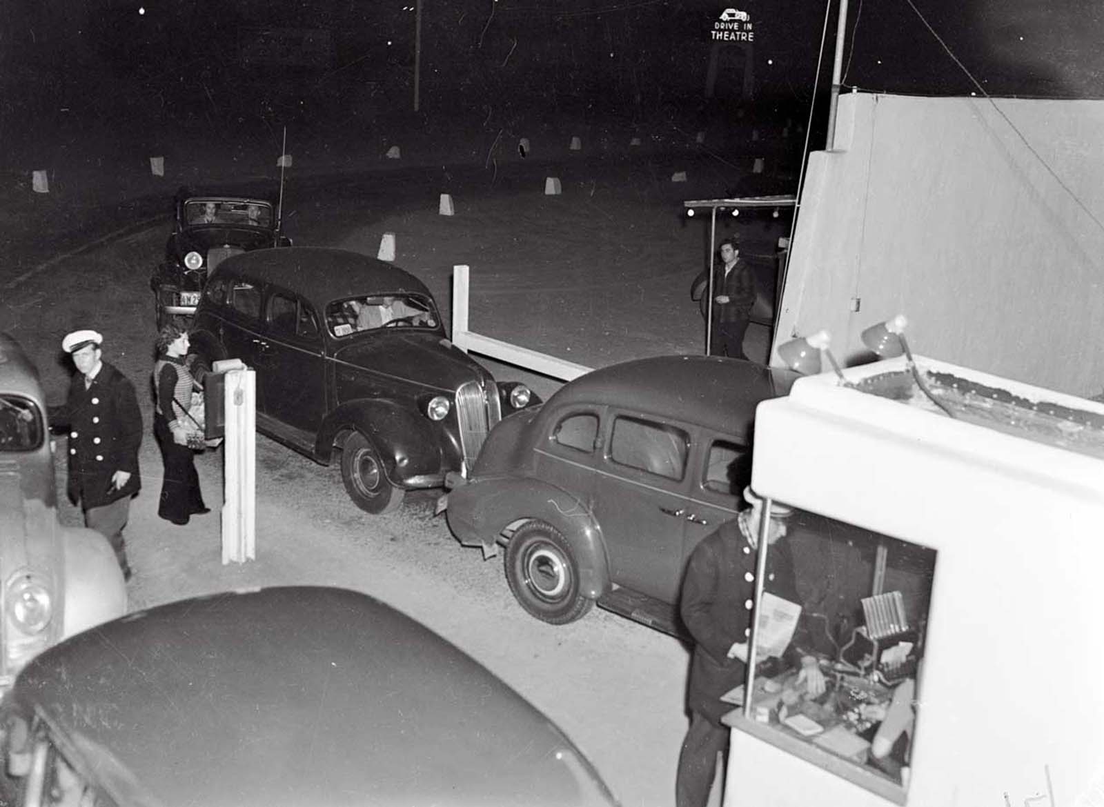 (Original Caption) The Cinemotor Theater. Los Angeles, Calif.: Motoring and motion pictures achieve a happy wedding in the Drive-In Theater in Los Angeles. The theater is a parking lot with graduated tiers from which motorists seated in their cars, watch the films projected on a giant screen. Synchronized amplifiers in the front of each car make speech audible in all parts of the lot. Here’s the entrance to the unique theater, showing the cashier’s wicket, and “butcher-girl” in front.
