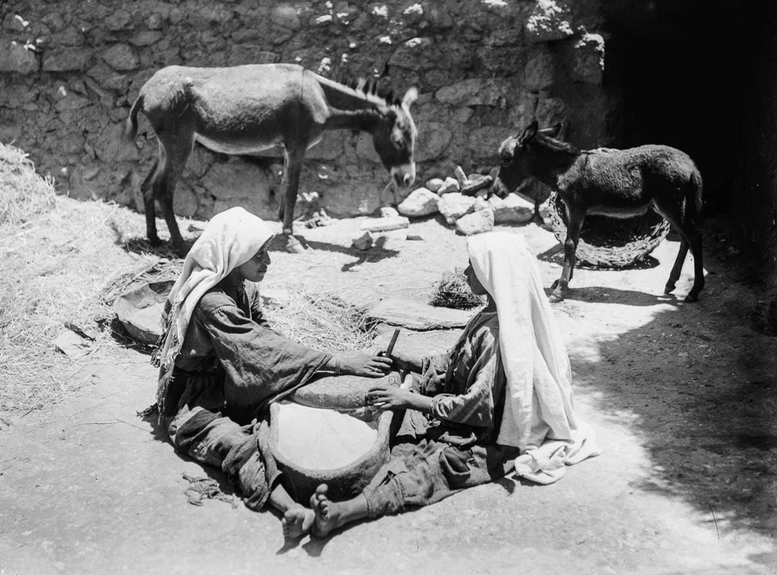 Two women work at a millstone.