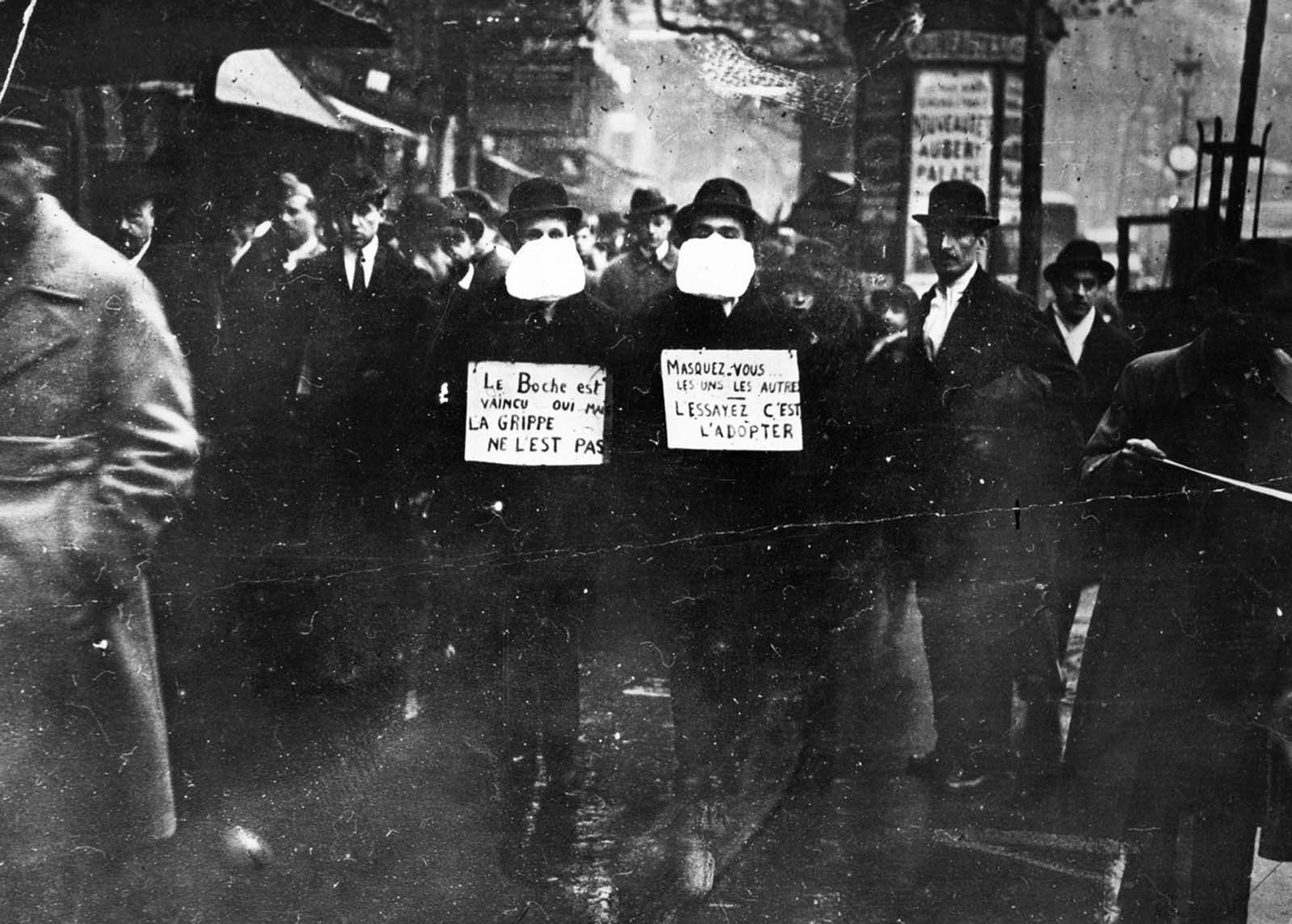 Two men wearing and advocating the use of flu masks in Paris, France. The signs translate roughly as: 