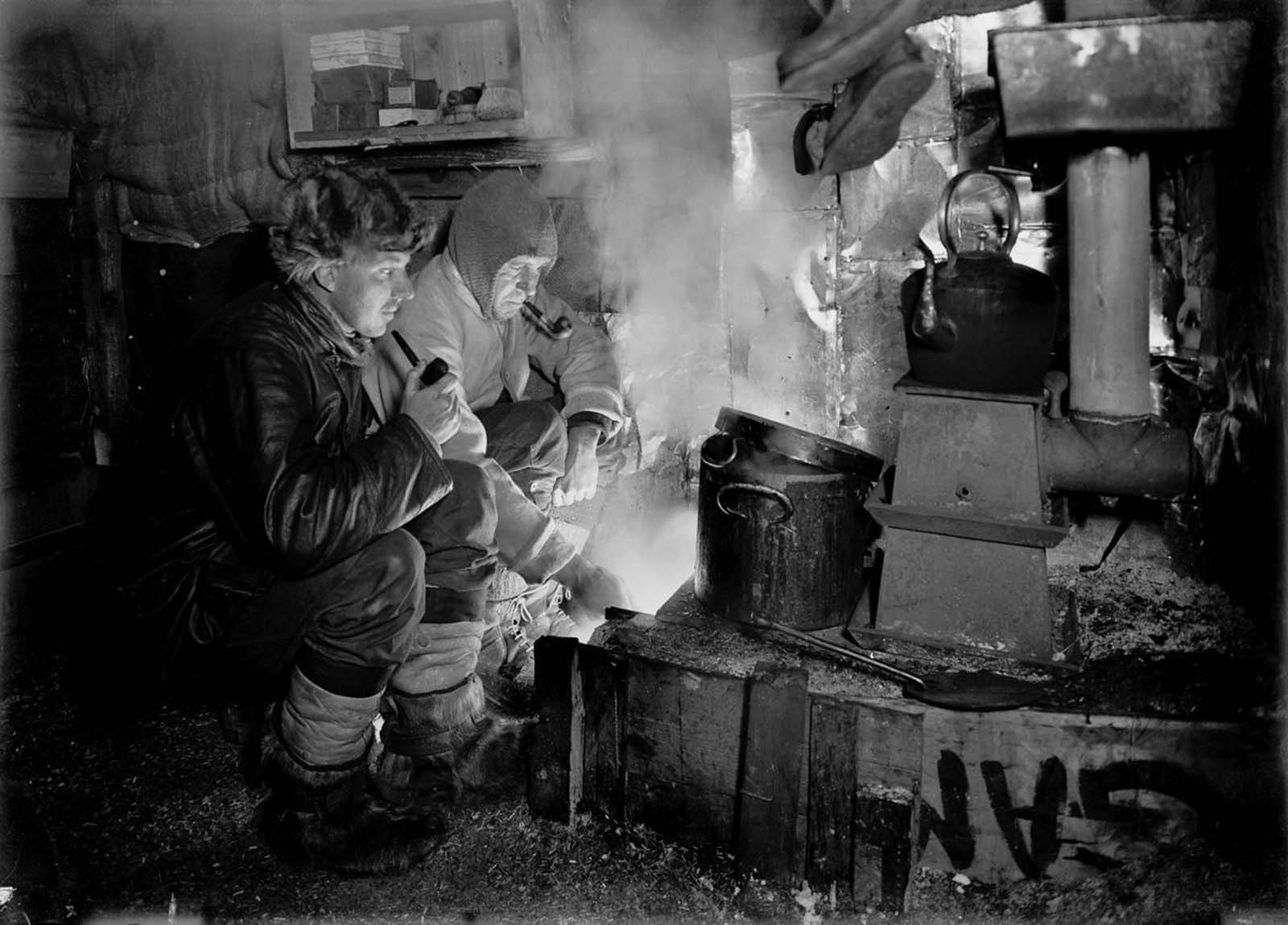 Dog handler Cecil Meares and Capt. Lawrence Oates cook blubber for the dogs. May, 1911.