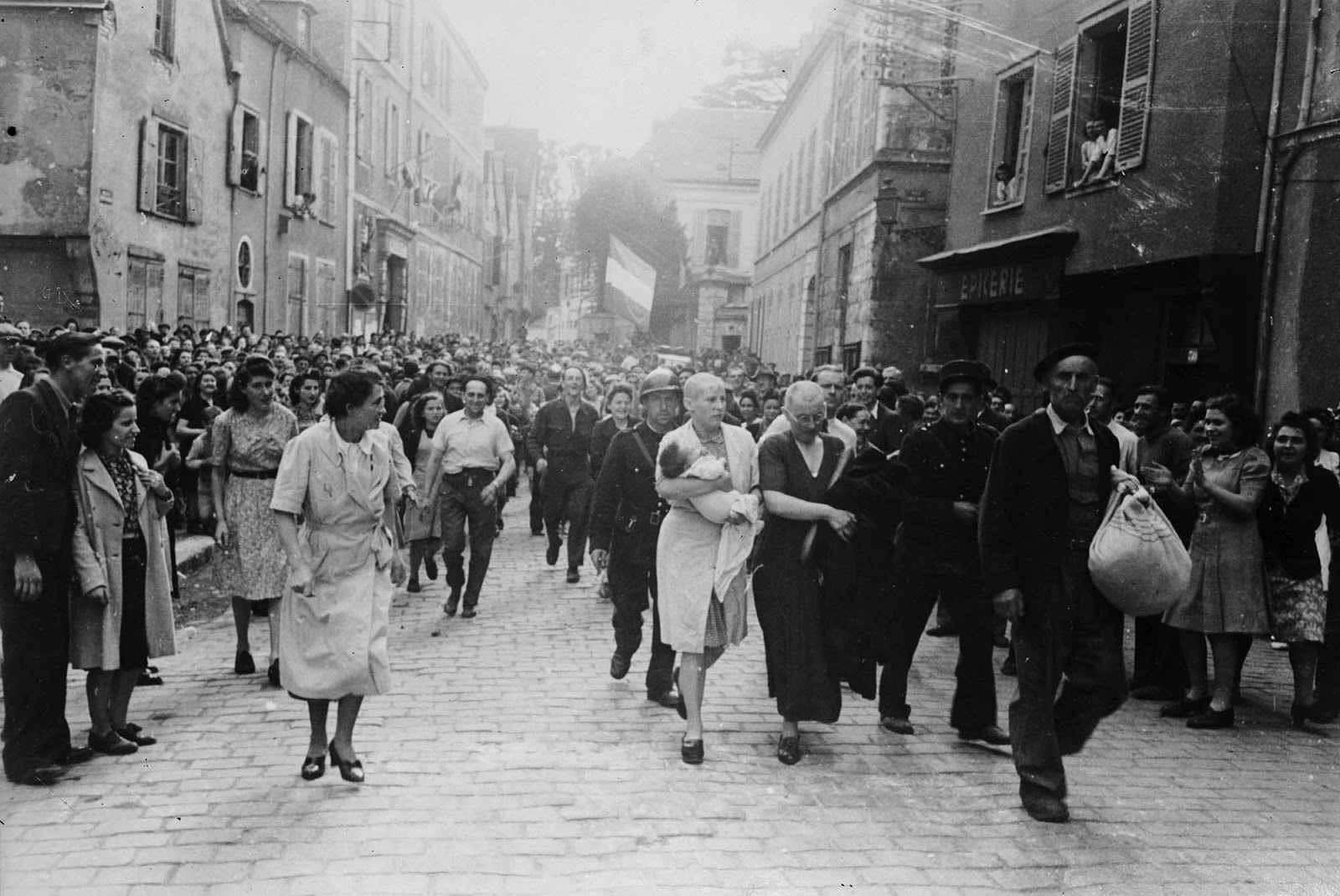 A woman, with her baby whose father is German, and her mother are jeered and humiliated by crowds in Chartres after having their heads shaved as punishment for collaborating with the German troops.